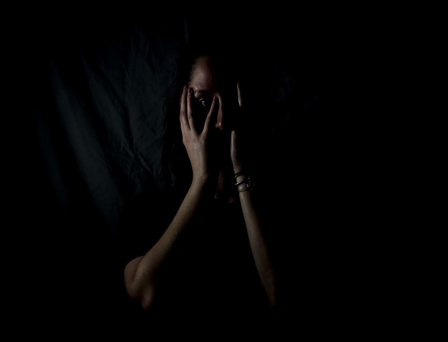 A woman peeks out from the shadows, looking scared. 