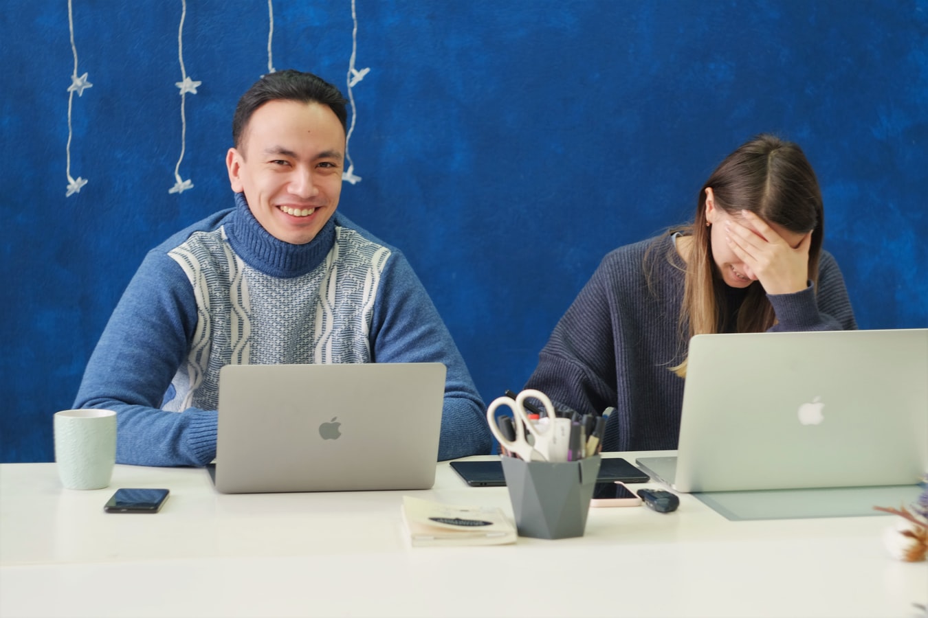 A man and a woman sit at their laptops laughing. 