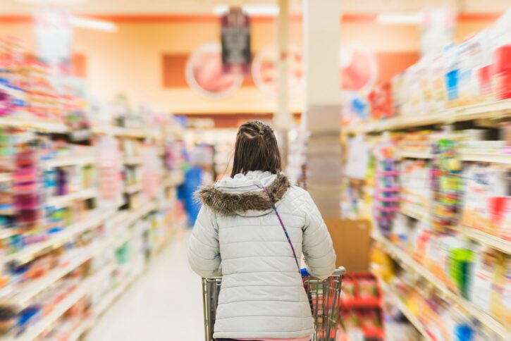 Grocery shopping, millennial woman in grocery store pushing cart through aisle